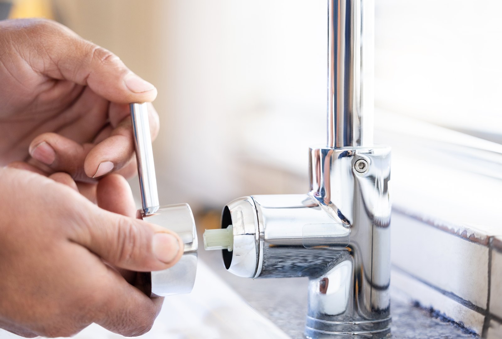 Illustrative close-up of hands working on a chrome mixer tap